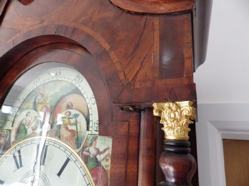 fig 4. An antique flame mahogany longcase clock featuring a painted dial, swan-neck pediment with brass finials, and spirally turned column detailing.