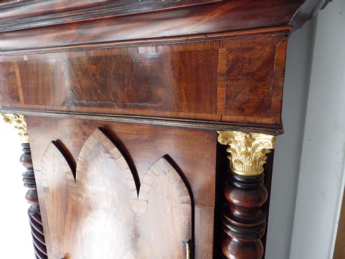 fig 5. An antique flame mahogany longcase clock featuring a painted dial, swan-neck pediment with brass finials, and spirally turned column detailing.