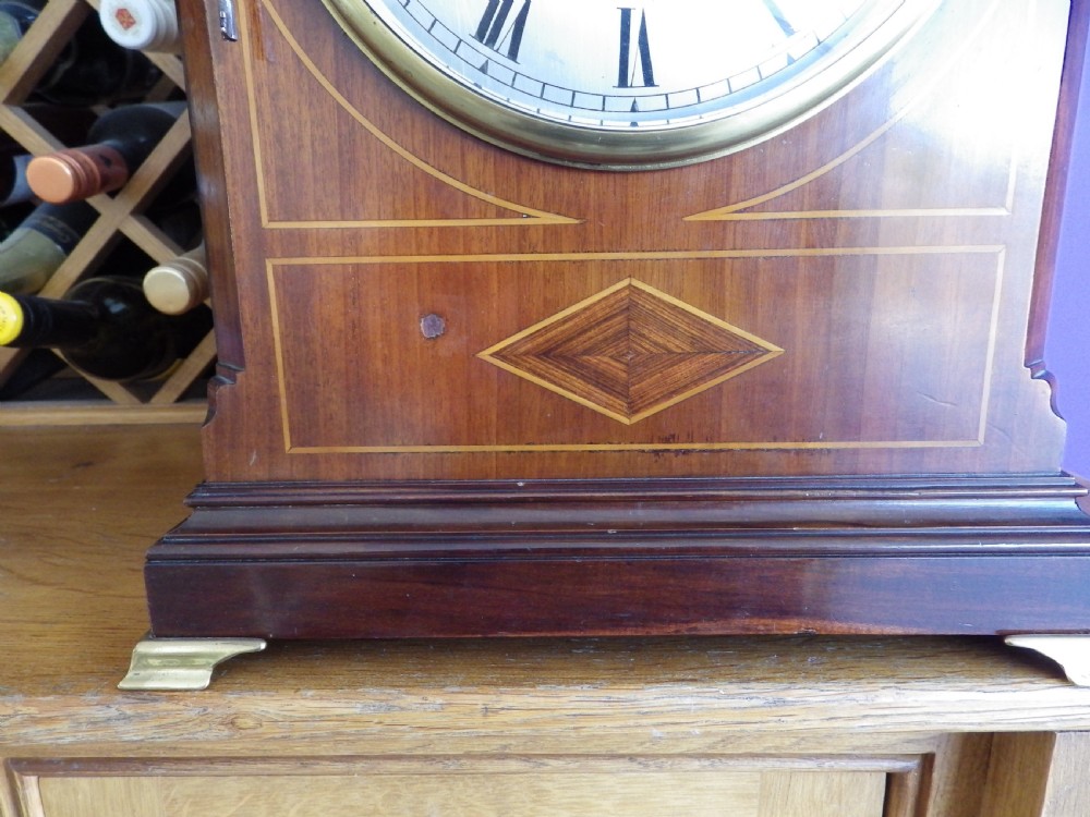 An antique mahogany arched pad-top bracket clock featuring satinwood stringing, a circular silvered dial with Roman numerals, and brass feet. View II