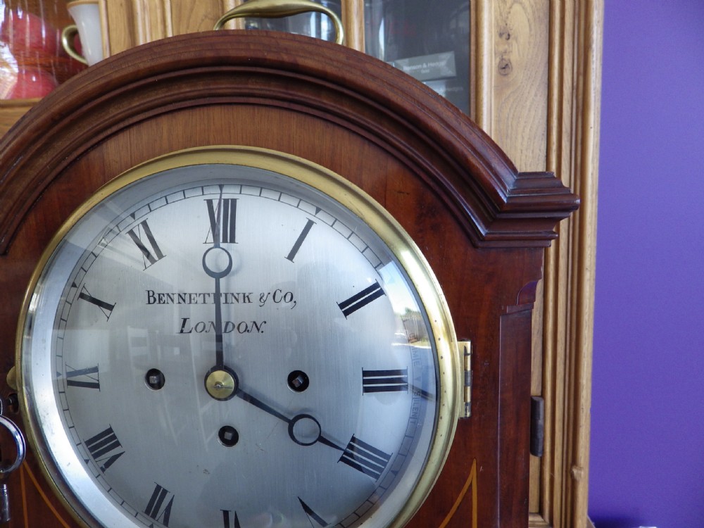 An antique mahogany arched pad-top bracket clock featuring satinwood stringing, a circular silvered dial with Roman numerals, and brass feet. View III