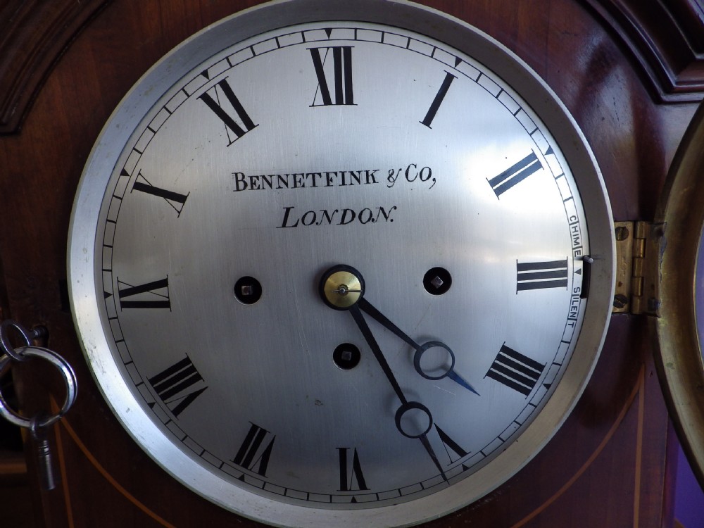 An antique mahogany arched pad-top bracket clock featuring satinwood stringing, a circular silvered dial with Roman numerals, and brass feet. View IV