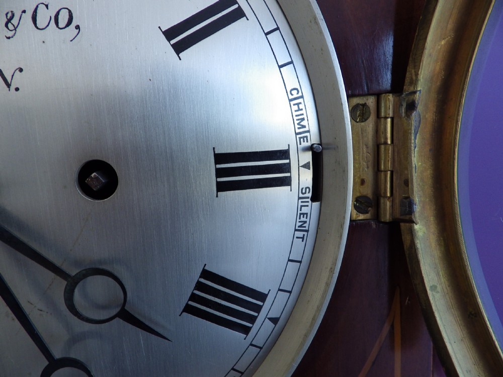 An antique mahogany arched pad-top bracket clock featuring satinwood stringing, a circular silvered dial with Roman numerals, and brass feet. View V