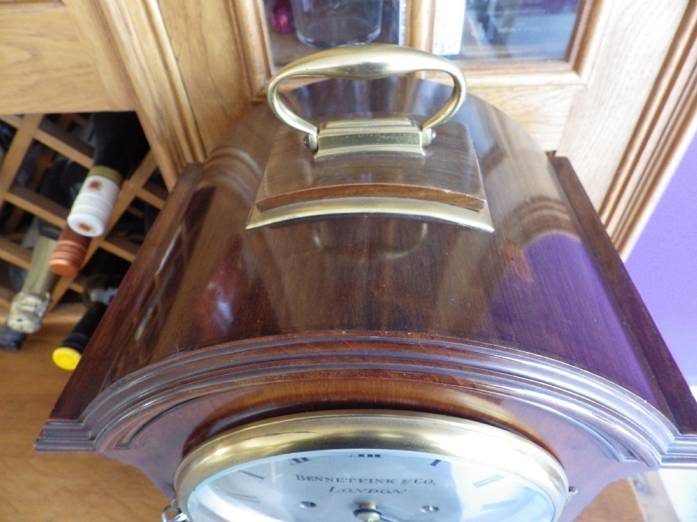 An antique mahogany arched pad-top bracket clock featuring satinwood stringing, a circular silvered dial with Roman numerals, and brass feet. View VI