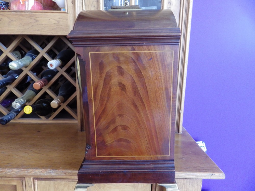An antique mahogany arched pad-top bracket clock featuring satinwood stringing, a circular silvered dial with Roman numerals, and brass feet. View VII