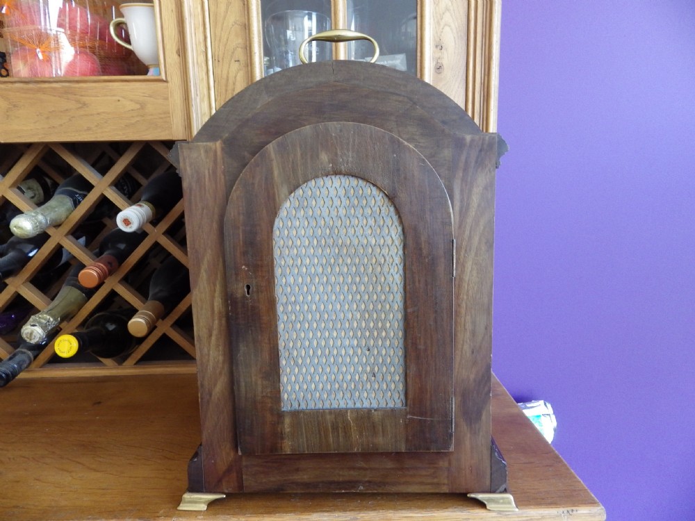 An antique mahogany arched pad-top bracket clock featuring satinwood stringing, a circular silvered dial with Roman numerals, and brass feet. View VIII