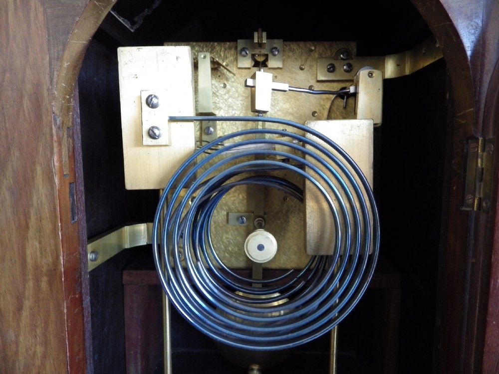 An antique mahogany arched pad-top bracket clock featuring satinwood stringing, a circular silvered dial with Roman numerals, and brass feet. View IX