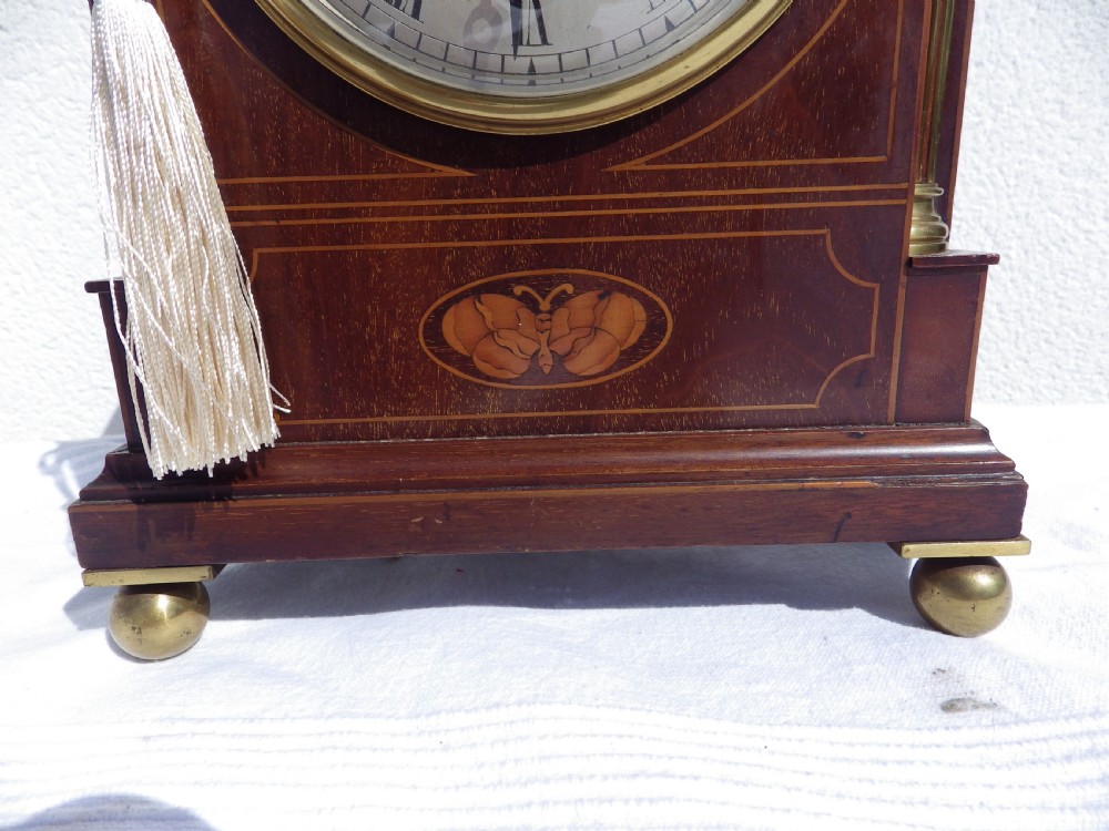An English double fusee bracket clock crafted from dark mahogany wood with brass finials, brass column accents, marquetry inlay, and a circular white dial featuring Roman numerals. View II
