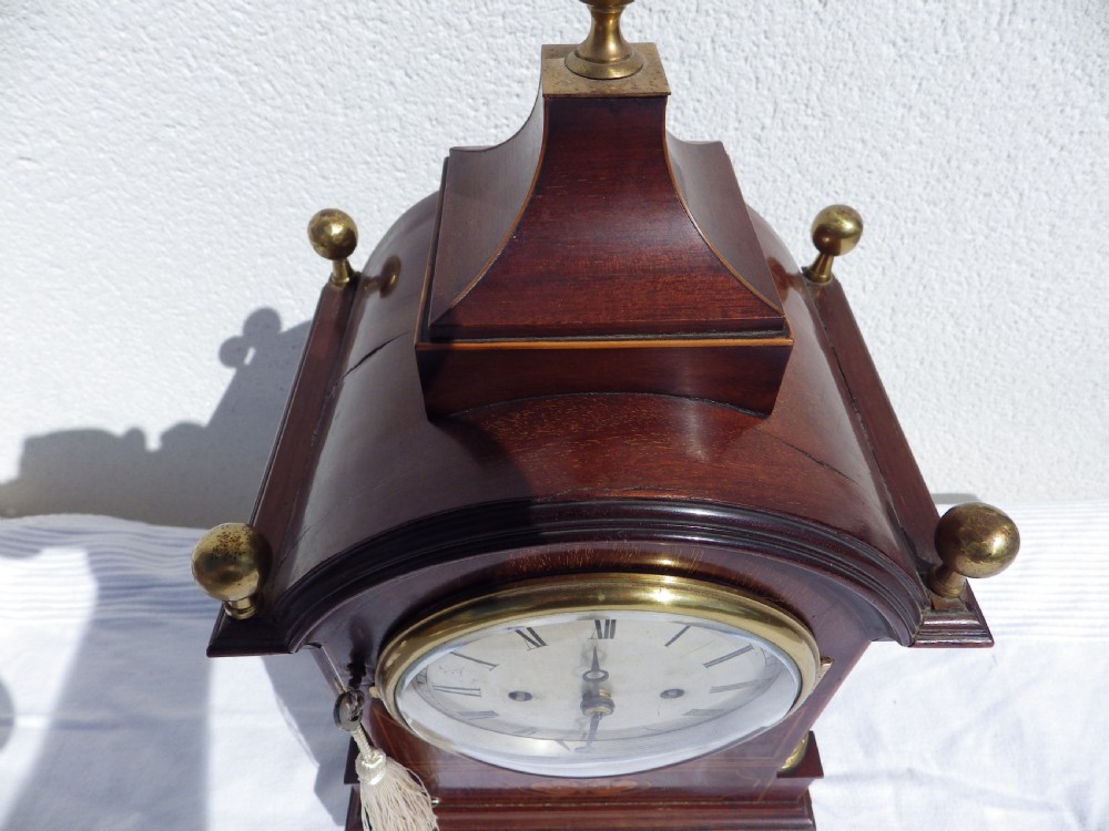 An English double fusee bracket clock crafted from dark mahogany wood with brass finials, brass column accents, marquetry inlay, and a circular white dial featuring Roman numerals. View III