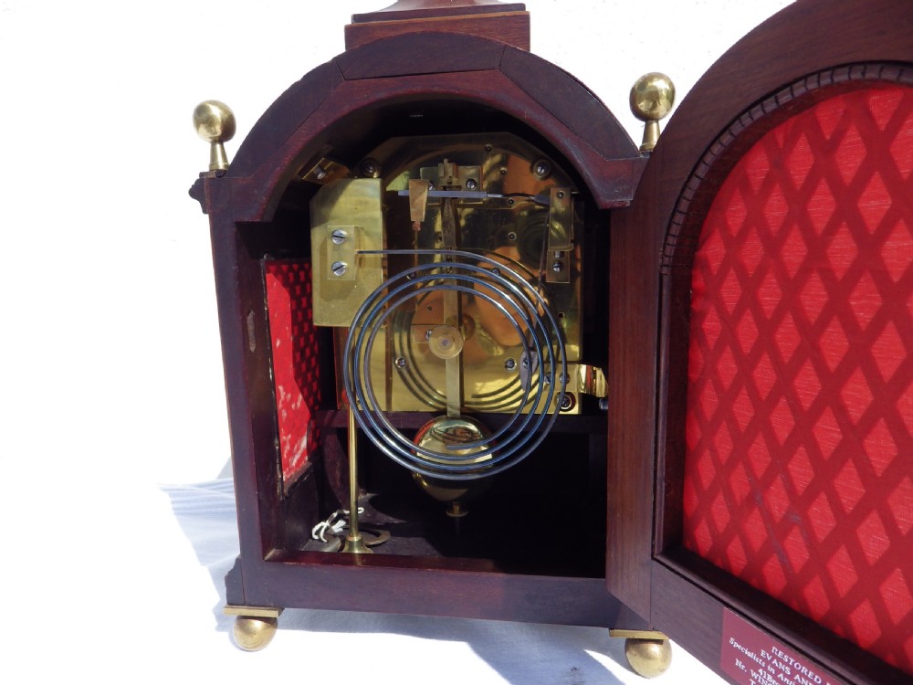 An English double fusee bracket clock crafted from dark mahogany wood with brass finials, brass column accents, marquetry inlay, and a circular white dial featuring Roman numerals. View VII
