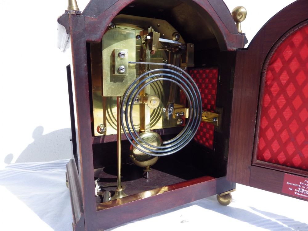 An English double fusee bracket clock crafted from dark mahogany wood with brass finials, brass column accents, marquetry inlay, and a circular white dial featuring Roman numerals. View VIII