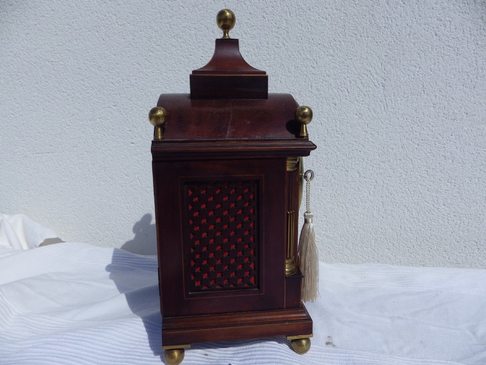 An English double fusee bracket clock crafted from dark mahogany wood with brass finials, brass column accents, marquetry inlay, and a circular white dial featuring Roman numerals. View IX