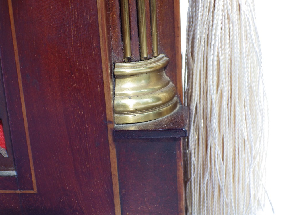 An English double fusee bracket clock crafted from dark mahogany wood with brass finials, brass column accents, marquetry inlay, and a circular white dial featuring Roman numerals. View X