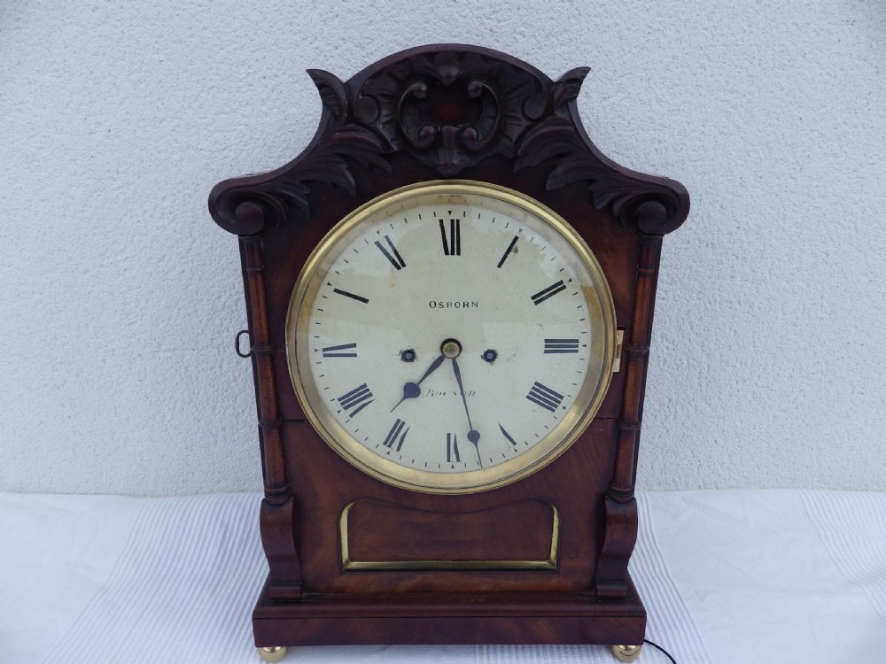 A carved mahogany English double fusee bracket clock featuring a circular cream dial with Roman numerals signed Osborn Bognor.