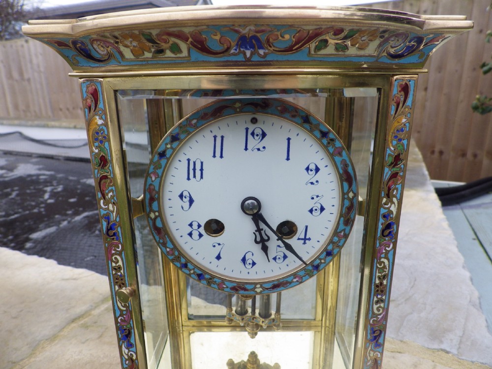 A late 19th-century French four-glass mantel clock featuring a brass frame, curved bow-front glass panel, polychrome champleve enamel borders, and a white porcelain dial with blue Arabic numerals. View III