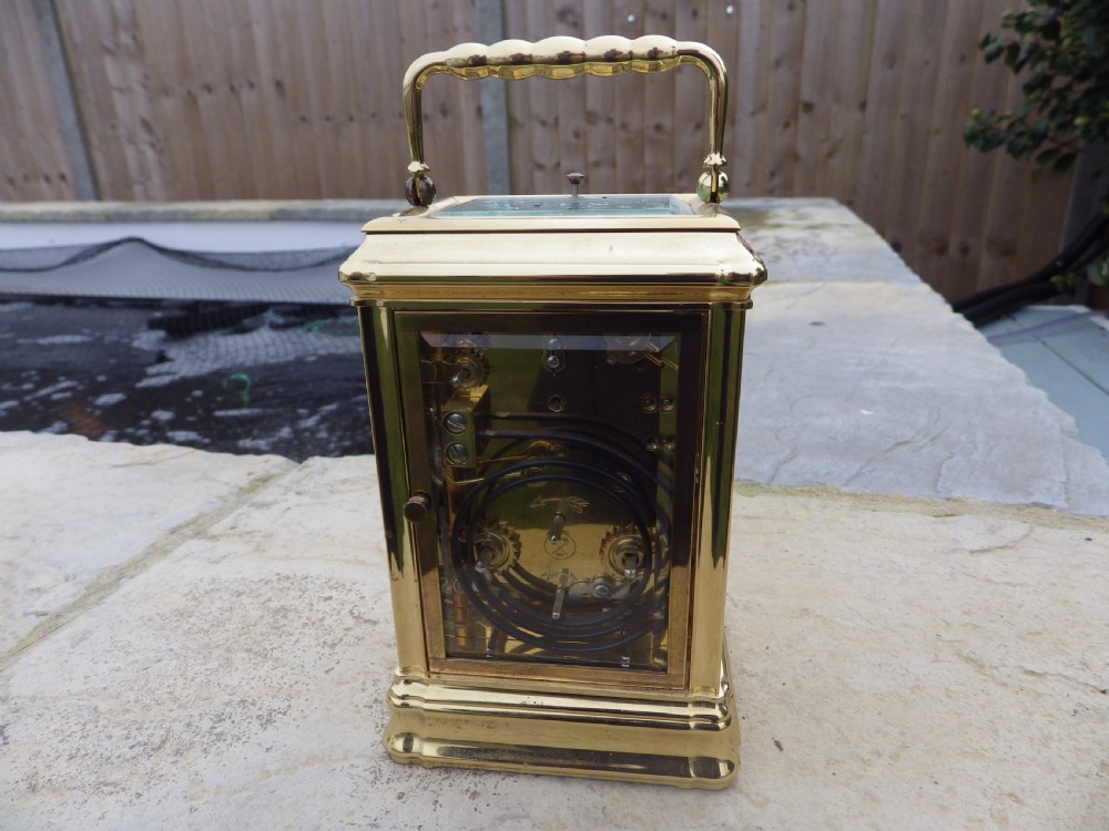 A polished brass LEpee carriage clock featuring bevelled glass panels, a white dial with Roman numerals, a moon phase aperture, and three subsidiary calendar dials. View IV