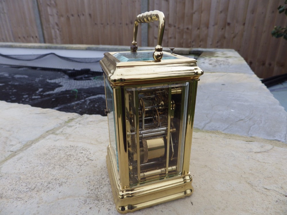 A polished brass LEpee carriage clock featuring bevelled glass panels, a white dial with Roman numerals, a moon phase aperture, and three subsidiary calendar dials. View V