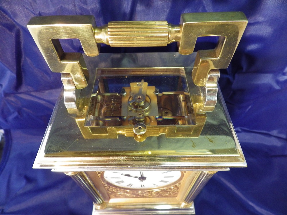 A nineteenth-century gilded brass French carriage clock featuring fluted corner columns, foliate engraving, a white enamel dial with Roman numerals, and a hinged carrying handle. View IV