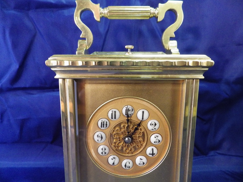 An antique brass French repeating carriage clock featuring an ornate circular dial with enamel numeral cartouches and a top carrying handle. View III