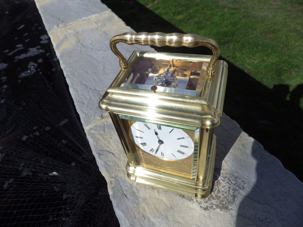 A French gilt brass giant repeating carriage clock featuring a white enamel dial with Roman numerals, an engraved brass mask, bevelled glass panels, and a hinged top handle. View II