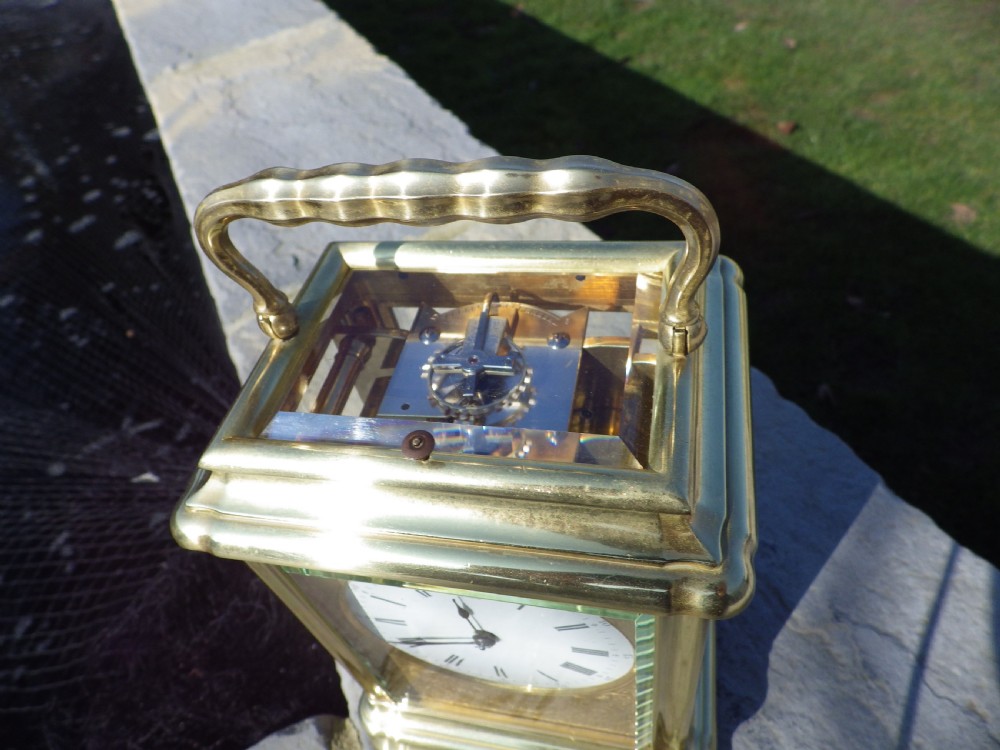A French gilt brass giant repeating carriage clock featuring a white enamel dial with Roman numerals, an engraved brass mask, bevelled glass panels, and a hinged top handle. View III