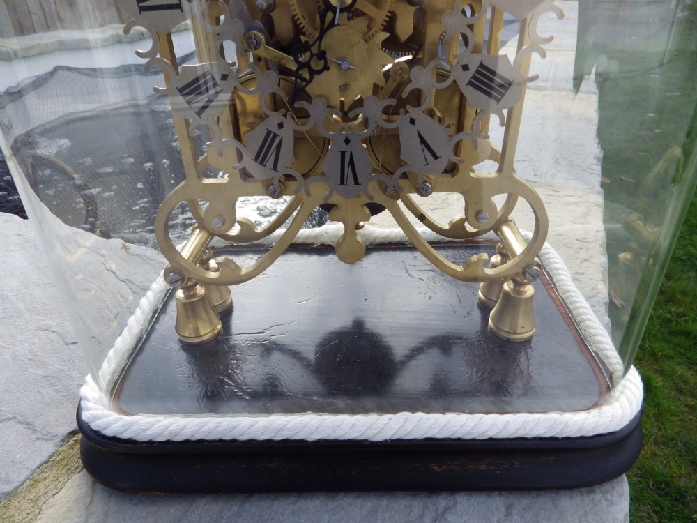 A Victorian brass double fusee skeleton clock with architectural Gothic spires and an openwork frame housed beneath a tall clear glass dome on an ebonised wooden base. View II