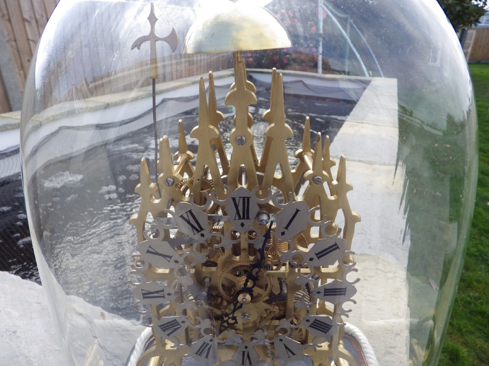A Victorian brass double fusee skeleton clock with architectural Gothic spires and an openwork frame housed beneath a tall clear glass dome on an ebonised wooden base. View III