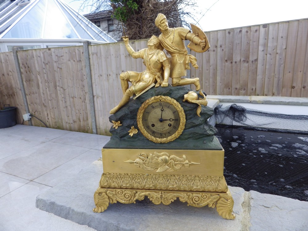An antique French Empire gilt and patinated bronze mantel clock featuring sculpted figures of medieval soldiers above an ornamented base.
