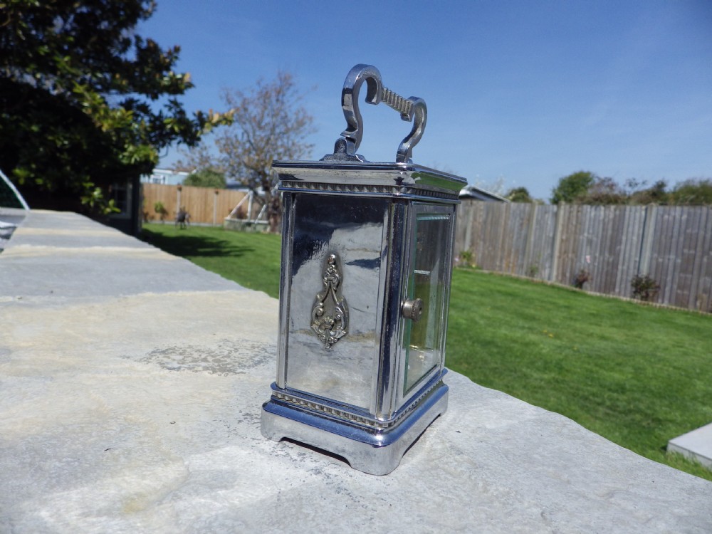 A silver-plated French carriage clock featuring a top carrying handle, a main white enamel dial with Roman numerals, and two subsidiary calendar dials set within a rectangular glass-panelled case. View II