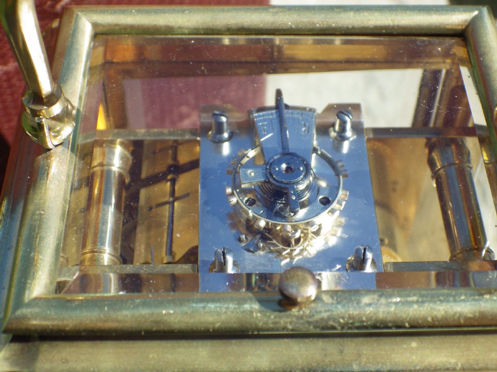 A late 19th-century French brass gorge case carriage clock with bevelled glass panels, a white enamel dial with Roman numerals, and a hinged brass carrying handle. View VI