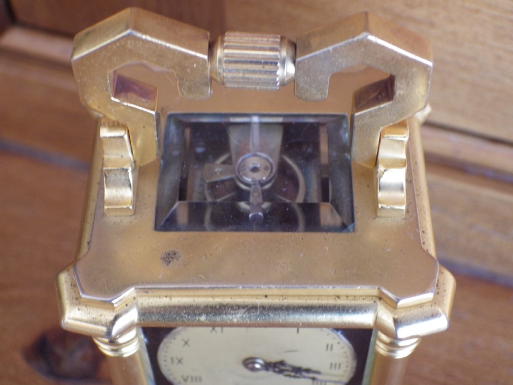 A French miniature gilt brass carriage clock featuring a stylized carrying handle, corner columns, and a black Limoges enamel face decorated with bird and floral painting. View V