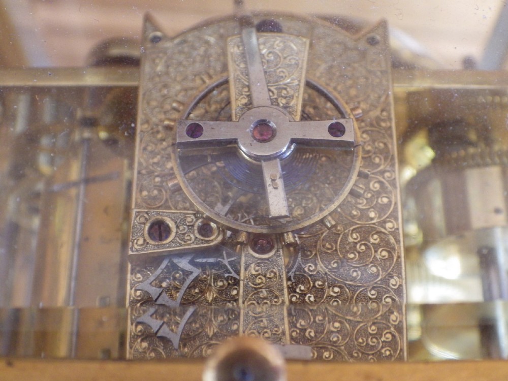 An antique gilt brass carriage clock featuring bevelled glass side panels, a top handle, a white enamel main dial with Roman numerals, and three subsidiary calendar dials below. View VI