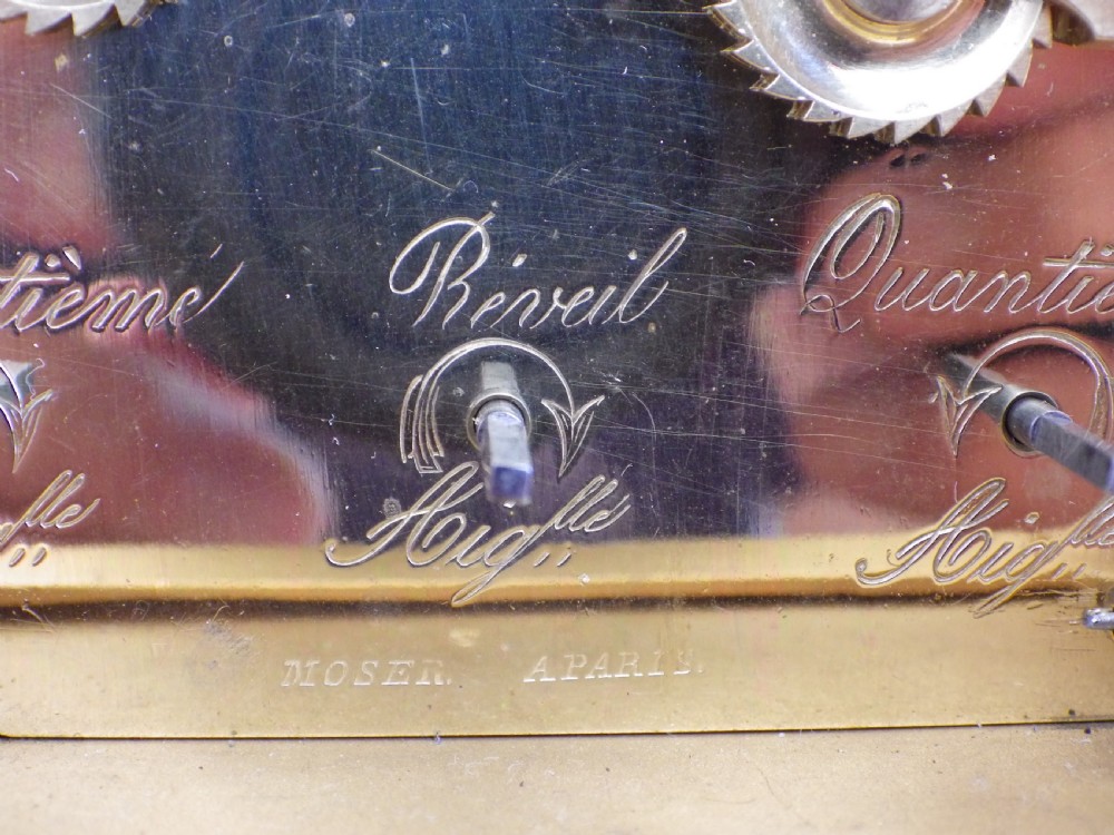 An antique gilt brass carriage clock featuring bevelled glass side panels, a top handle, a white enamel main dial with Roman numerals, and three subsidiary calendar dials below. View IX