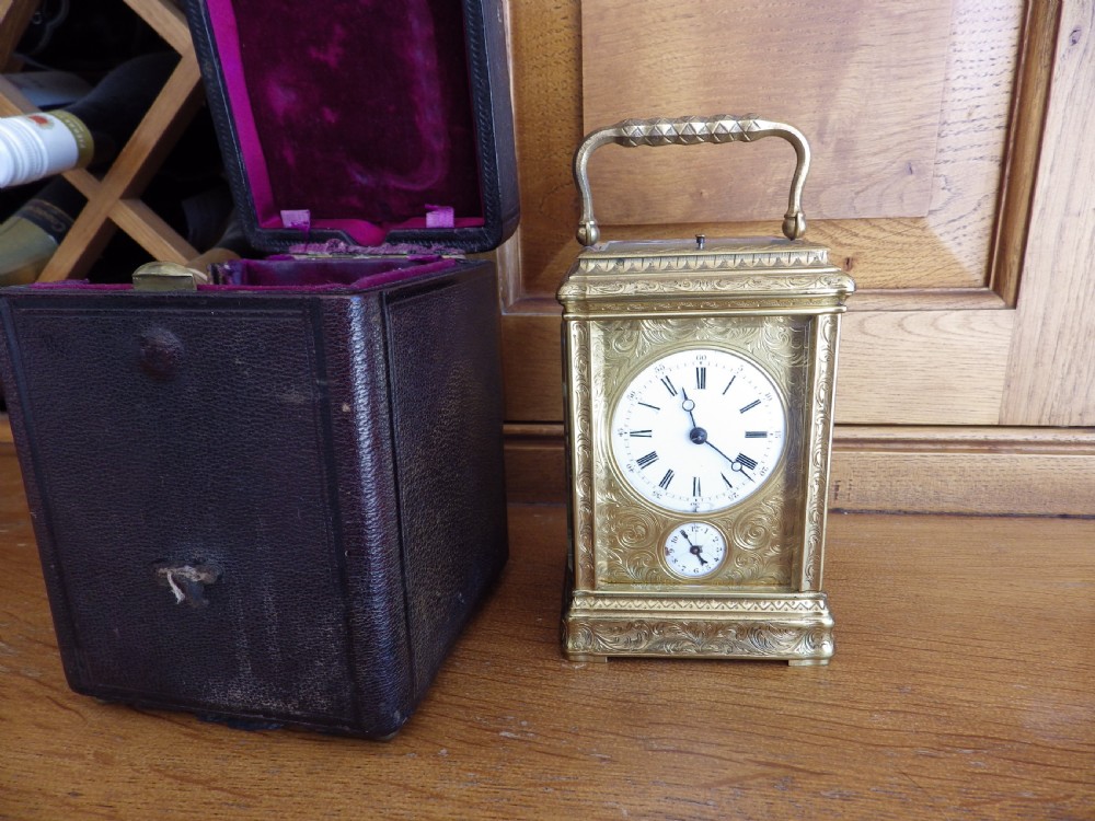 An 1870s French gilt brass repeating carriage clock featuring a fully hand-engraved case, white enamel dial with Roman numerals, and a hinged carrying handle.