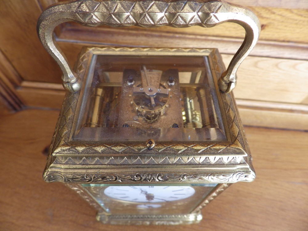 An 1870s French gilt brass repeating carriage clock featuring a fully hand-engraved case, white enamel dial with Roman numerals, and a hinged carrying handle. View VI