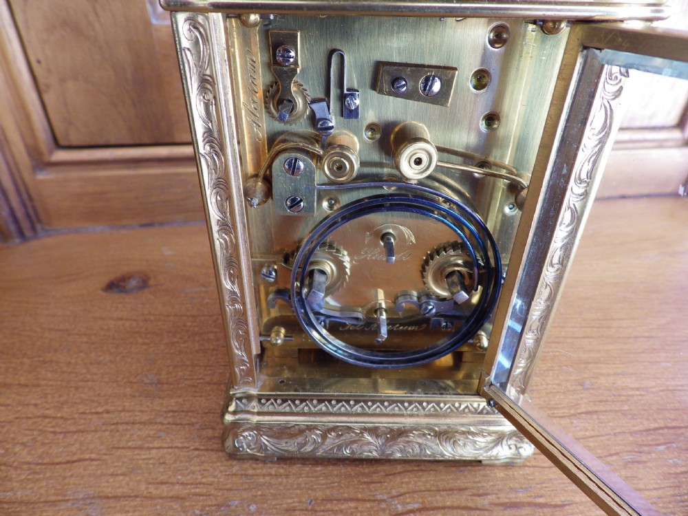 An 1870s French gilt brass repeating carriage clock featuring a fully hand-engraved case, white enamel dial with Roman numerals, and a hinged carrying handle. View VII