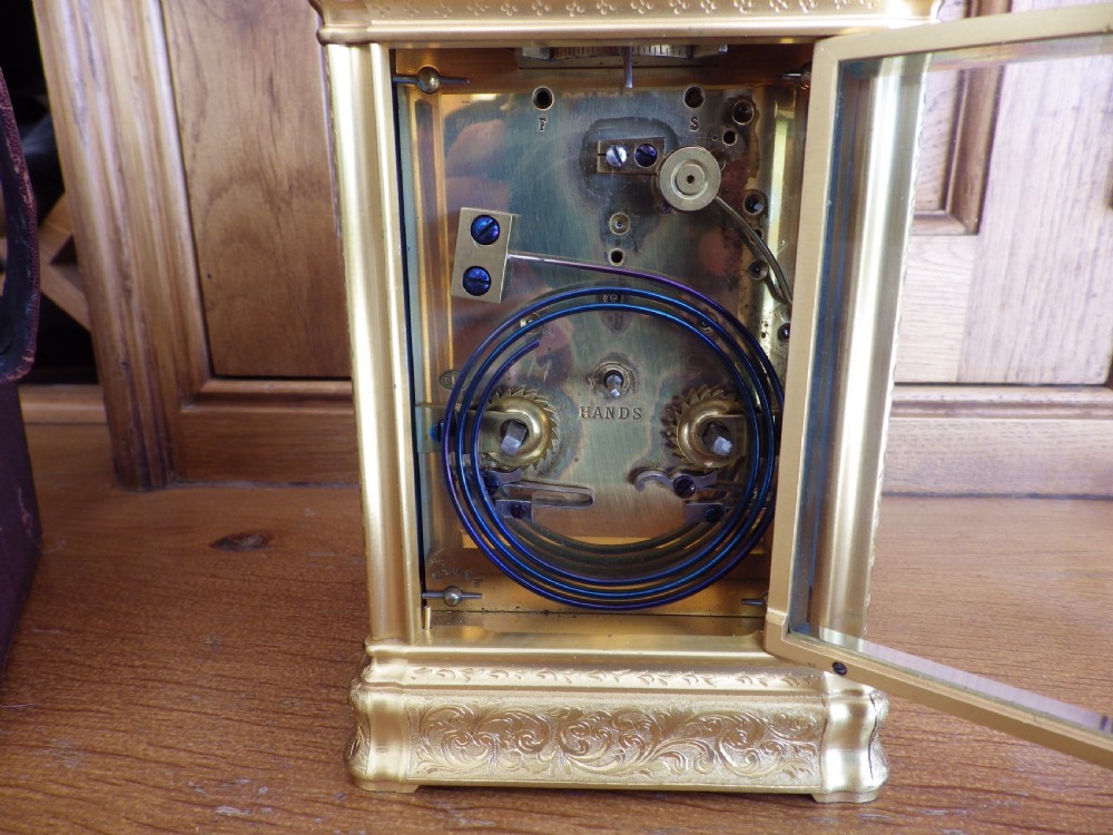 A rectangular gilt brass carriage clock with a hinged handle, featuring a painted enamel dial with Roman numeral cartouches and a scene depicting a figure seated in a garden setting. View V