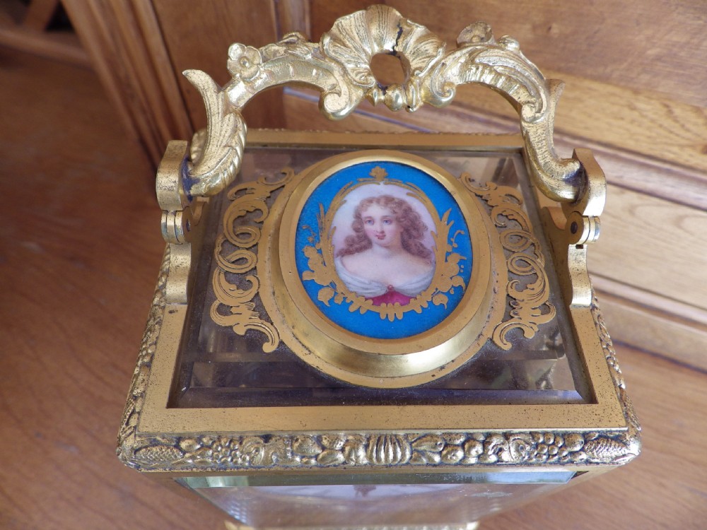 A French gilt brass carriage clock with an ornate foliate engraved face panel, white enamel dial with Roman numerals, secondary sub-dial, and decorative top handle. View IV