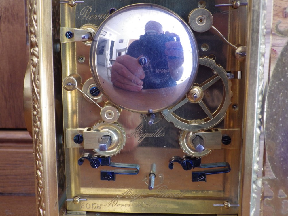 A French gilt brass carriage clock with an ornate foliate engraved face panel, white enamel dial with Roman numerals, secondary sub-dial, and decorative top handle. View IX