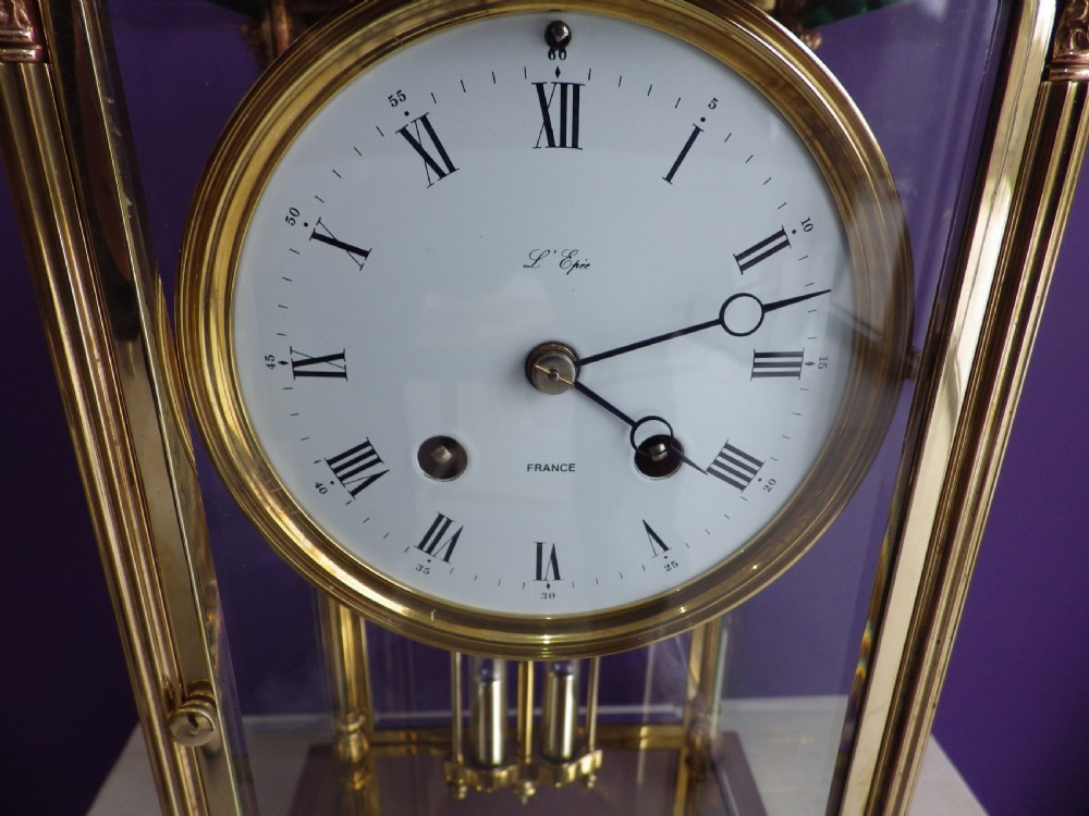 A brass French crystal regulator mantle clock featuring four bevelled glass sides, fluted corner columns, a white enamel dial with Roman numerals, and a visible pendulum. View VI