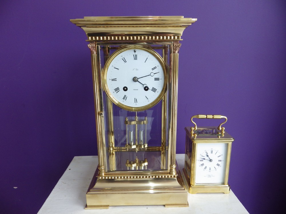 A brass French crystal regulator mantle clock featuring four bevelled glass sides, fluted corner columns, a white enamel dial with Roman numerals, and a visible pendulum. View VII