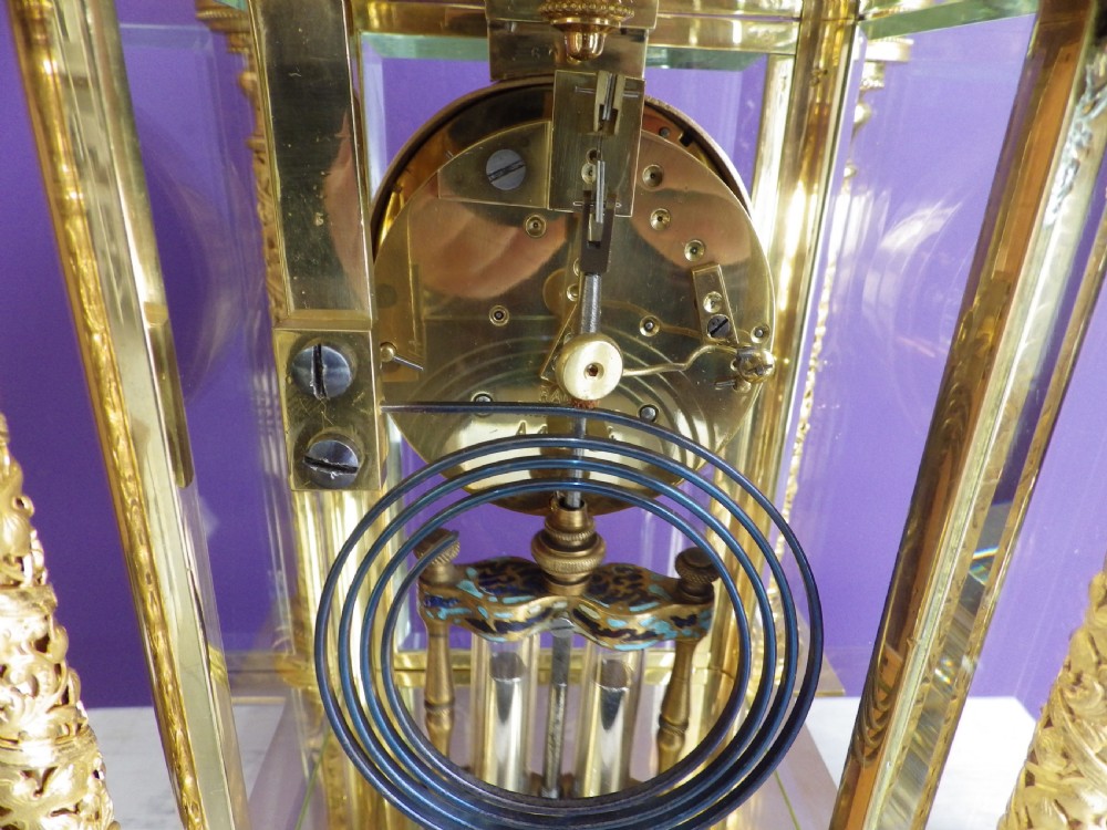 An antique French gilt brass crystal regulator clock featuring four clear glass sides, blue champleve enamel scrollwork, decorative corner columns, and an intricate dial. View VII