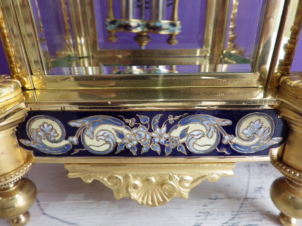 An antique French gilt brass crystal regulator clock featuring four clear glass sides, blue champleve enamel scrollwork, decorative corner columns, and an intricate dial. View XI