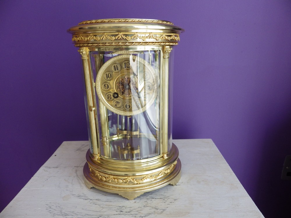 A French oval gilt brass crystal regulator clock featuring bevelled glass casing, fluted column supports, and an ornate circular dial.