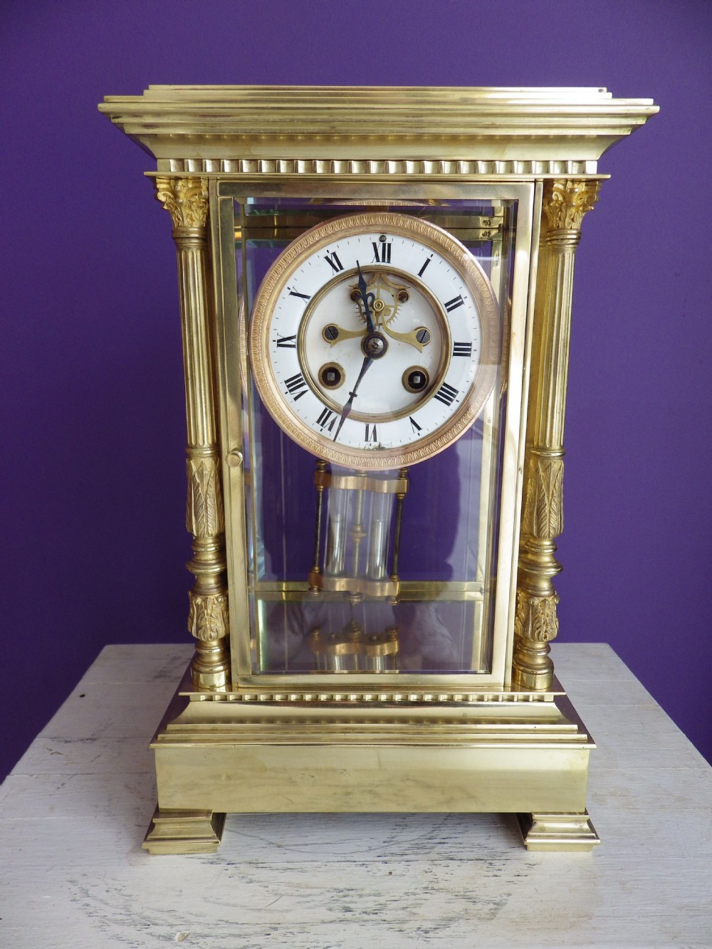 A nineteenth-century French gilt brass crystal regulator mantel clock featuring four bevelled glass sides, fluted corner columns, an enamel dial with Roman numerals, and a visible pendulum.