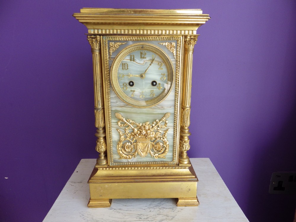 A late 19th-century French gilt bronze mantle clock featuring green onyx panels, fluted side columns, and an ornate floral mount.