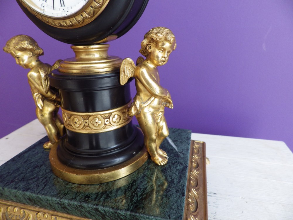 An 1880s French mantel clock featuring two gilt winged cherubs beside a central black column with a white enamel dial, set upon a green marble plinth with gilt feet. View II