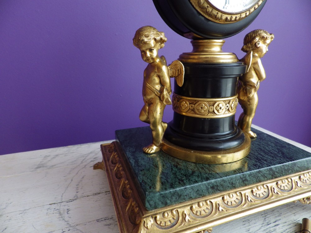An 1880s French mantel clock featuring two gilt winged cherubs beside a central black column with a white enamel dial, set upon a green marble plinth with gilt feet. View III