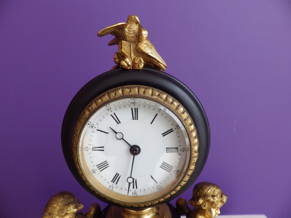 An 1880s French mantel clock featuring two gilt winged cherubs beside a central black column with a white enamel dial, set upon a green marble plinth with gilt feet. View IV