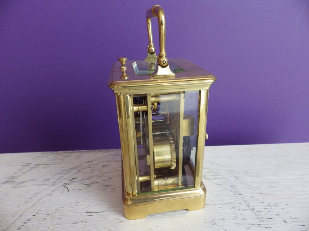 A brass French carriage clock featuring clear glass side panels, a white enamel dial with black numerals, and a hinged brass carrying handle. View II