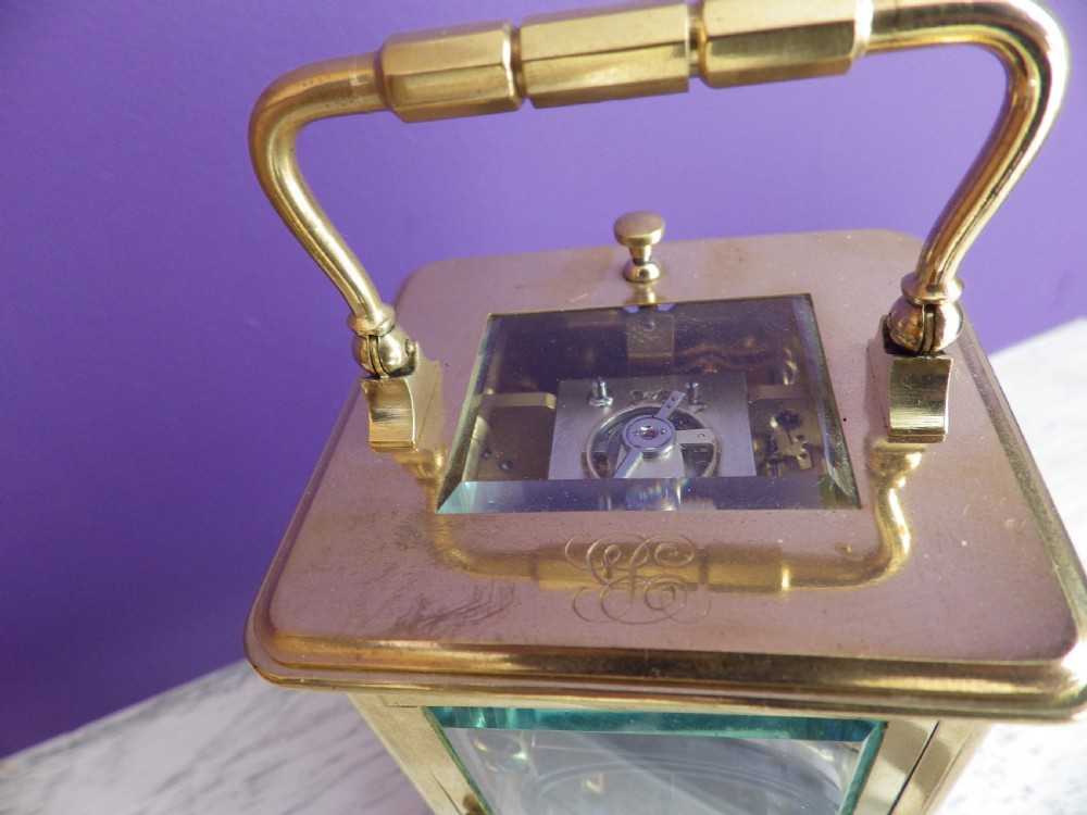 A brass French carriage clock featuring clear glass side panels, a white enamel dial with black numerals, and a hinged brass carrying handle. View V